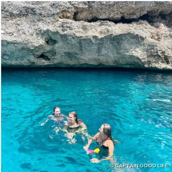 Guests swimming in bright blue water in front of a cliff cave